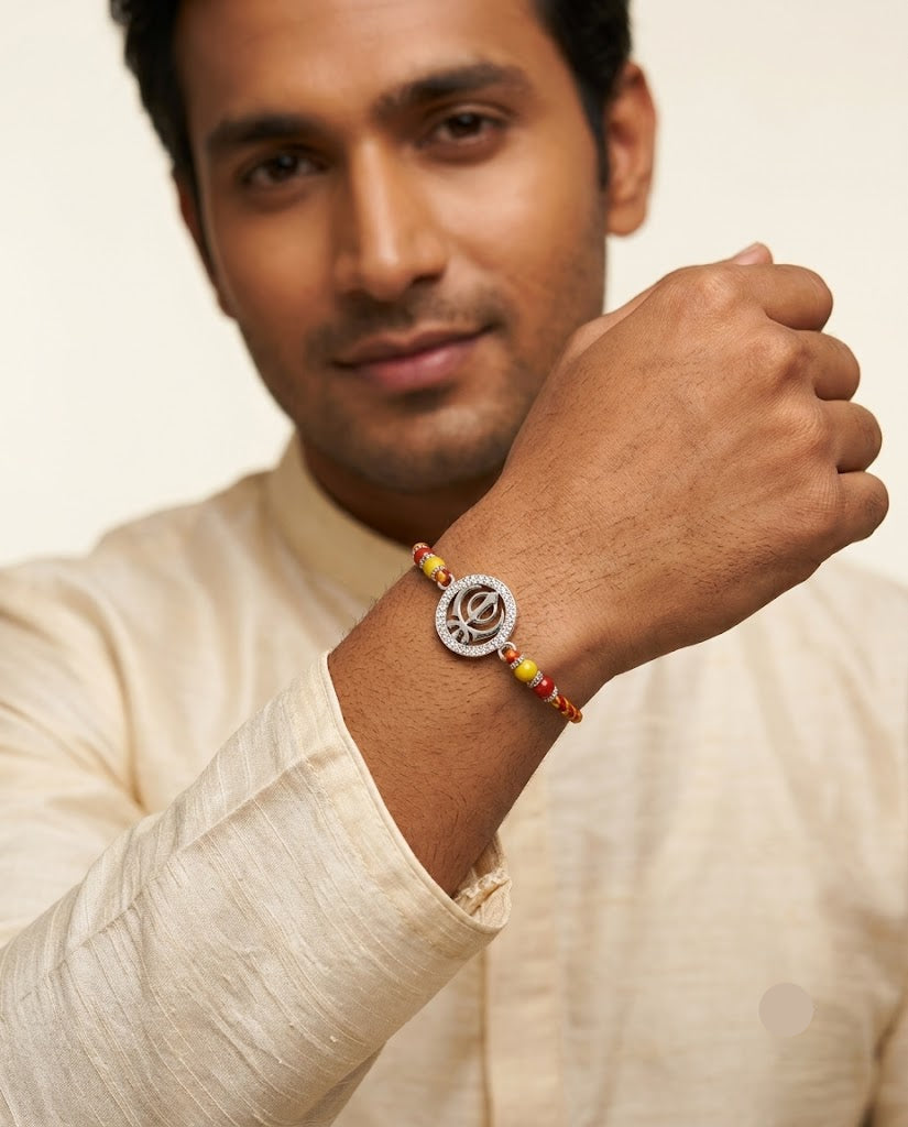 A man wearing a traditional Indian rakhi bracelet with a silver-tone circular pendant and red and yellow beaded cord, shown in a close-up lifestyle shot.