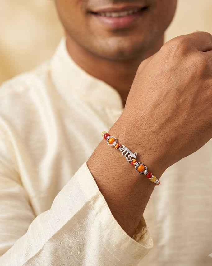 A close-up of a man wearing a beaded bracelet on his wrist, dressed in a cream-colored shirt against a soft beige background.