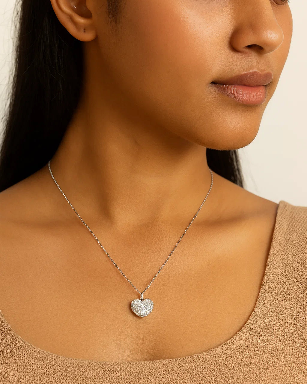 Woman wearing a silver heart-shaped pendant necklace against a neutral background