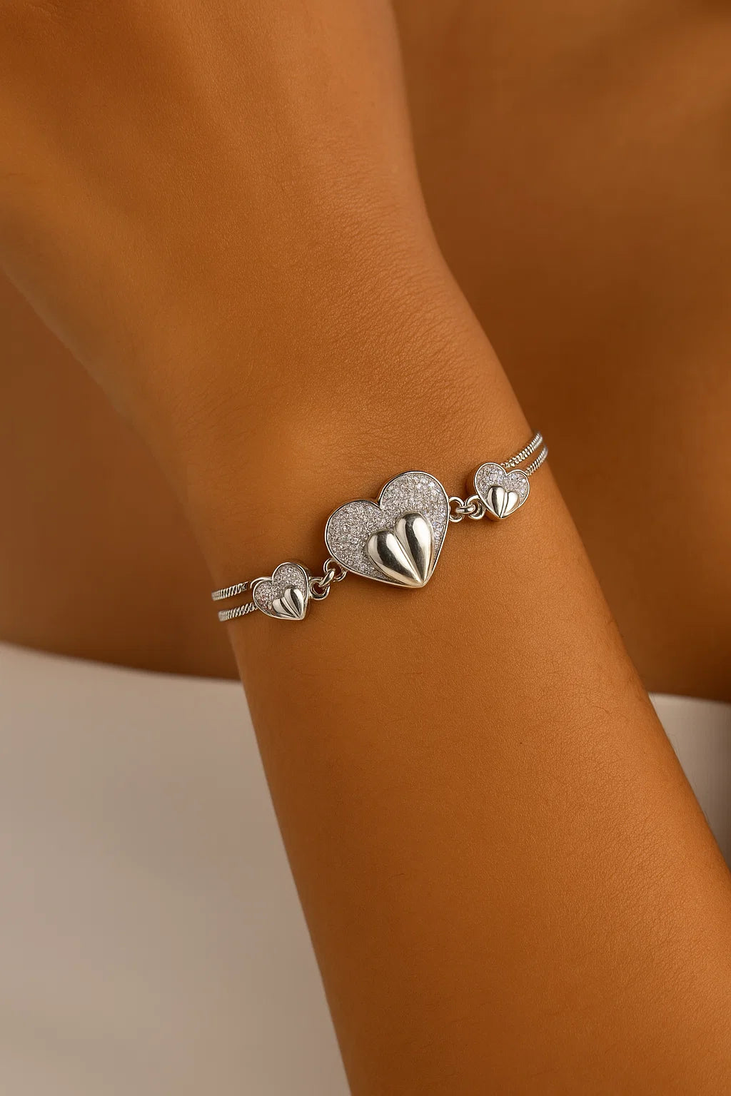 Silver bracelet with heart-shaped charms on a wrist against a brown background