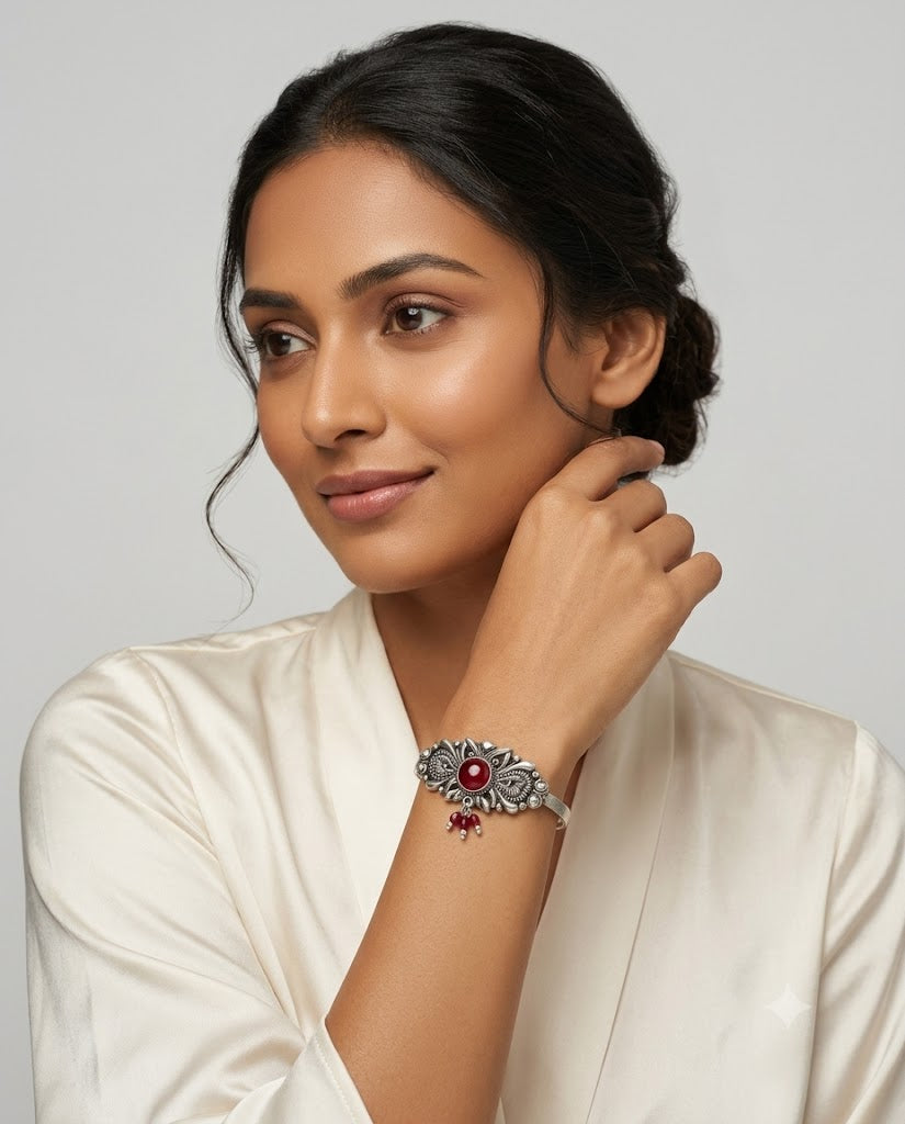 Woman wearing a silver bracelet with a red gemstone on a plain background