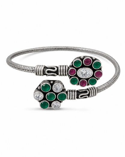 Silver bracelet with green and red gemstone accents on a white background