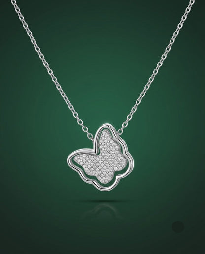A silver butterfly pendant necklace with a textured pavé center, suspended from a delicate silver chain against a dark green gradient background.