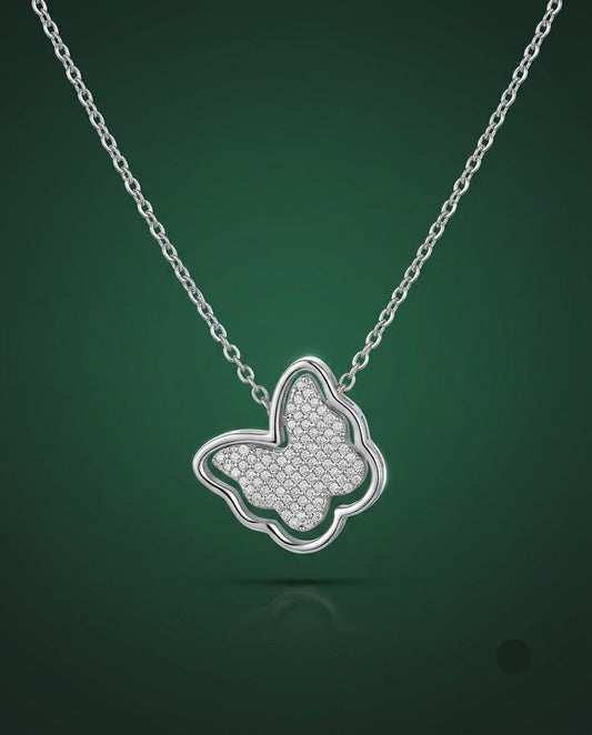 A silver butterfly pendant necklace with a textured pavé center, suspended from a delicate silver chain against a dark green gradient background.