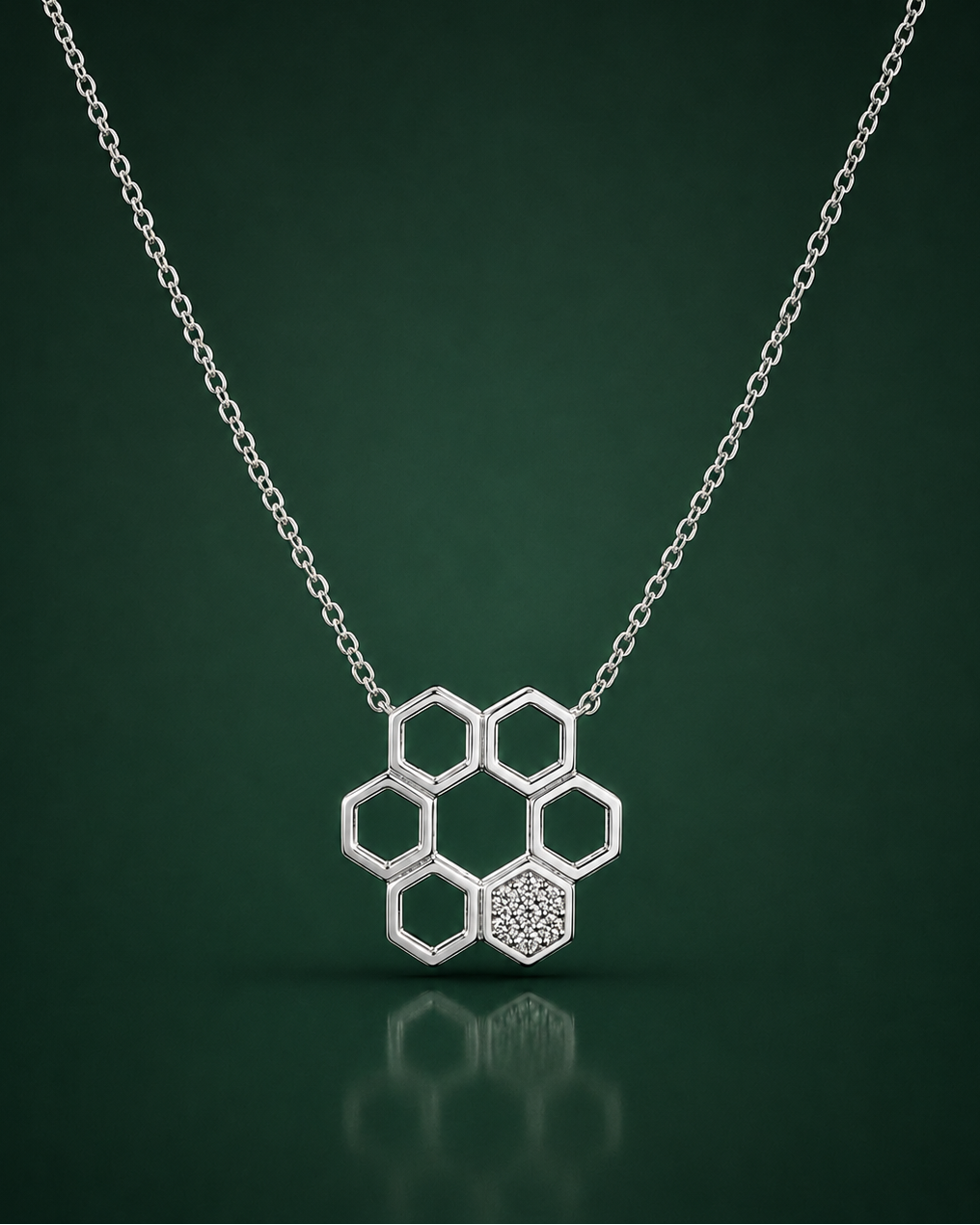 A silver honeycomb pendant necklace with one textured hexagon and five open hexagons, suspended from a delicate silver chain against a dark green gradient background.