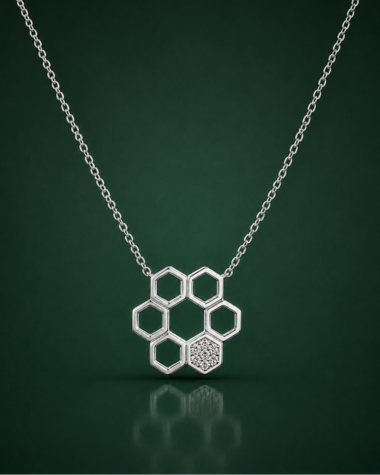 A silver honeycomb pendant necklace with one textured hexagon and five open hexagons, suspended from a delicate silver chain against a dark green gradient background.