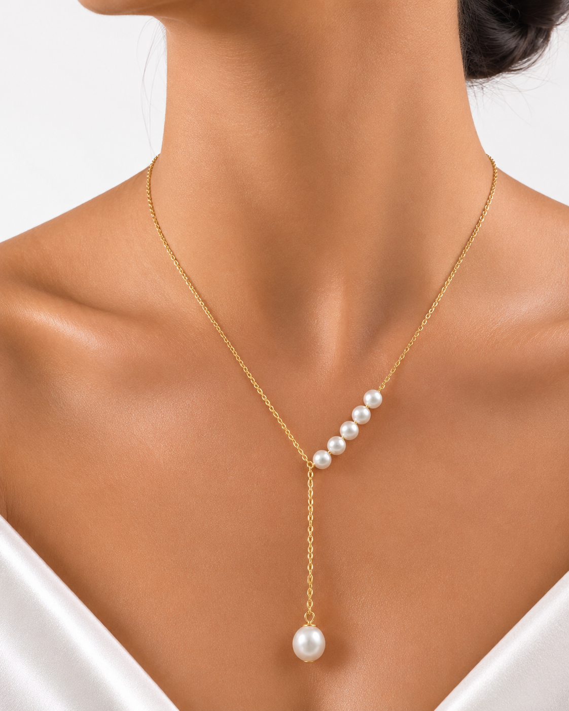 A gold Y-necklace with a row of white pearls and a single dangling pearl pendant, shown on a model's neck and upper chest.