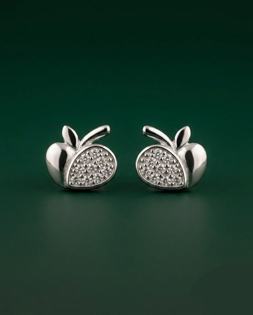 A pair of silver apple-shaped stud earrings with pavé-set clear stones on the front, displayed on a dark green background.