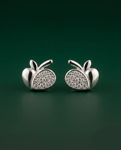 A pair of silver apple-shaped stud earrings with pavé-set clear stones on the front, displayed on a dark green background.