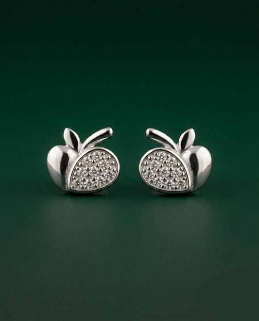 A pair of silver apple-shaped stud earrings with pavé-set clear stones on the front, displayed on a dark green background.