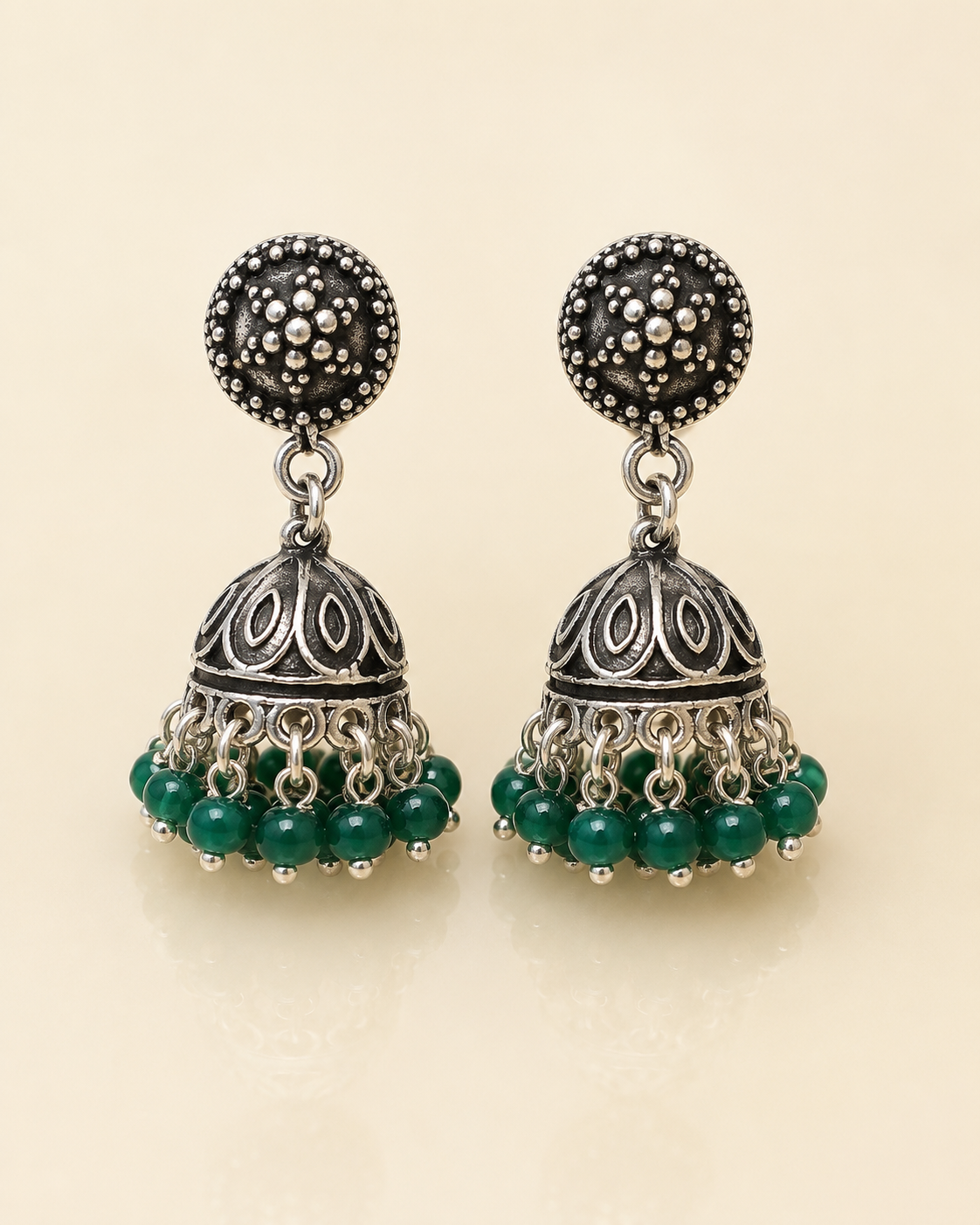 A pair of traditional Indian silver jhumka earrings with dark green bead fringe, displayed on a light beige background.