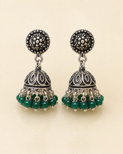 A pair of traditional Indian silver jhumka earrings with dark green bead fringe, displayed on a light beige background.