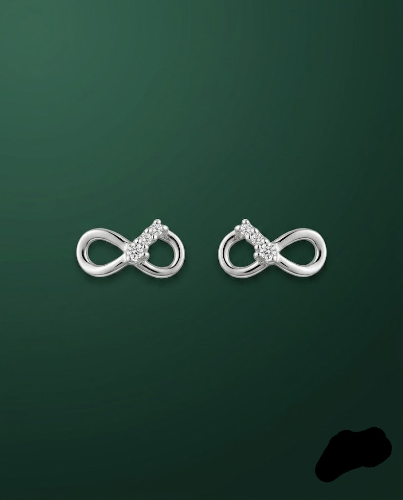 A pair of silver infinity-shaped stud earrings with small clear gemstone clusters at the center, displayed on a dark green gradient background.
