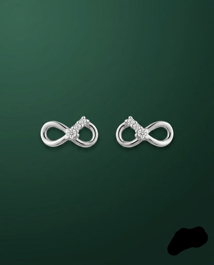A pair of silver infinity-shaped stud earrings with small clear gemstone clusters at the center, displayed on a dark green gradient background.