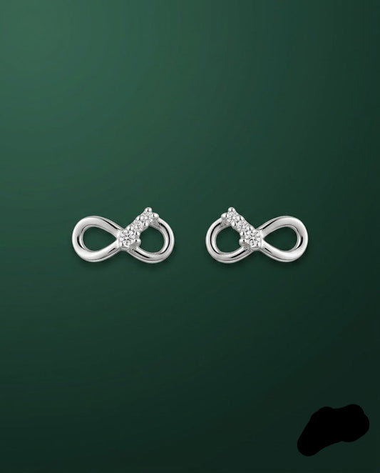 A pair of silver infinity-shaped stud earrings with small clear gemstone clusters at the center, displayed on a dark green gradient background.