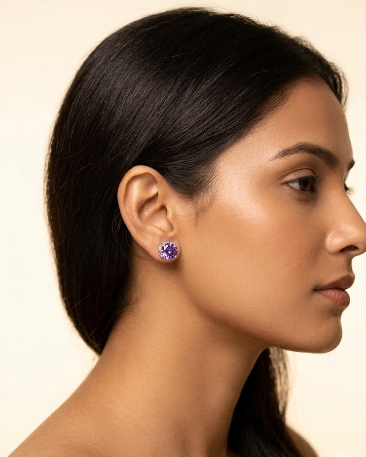 Woman wearing purple gemstone earrings against a beige background