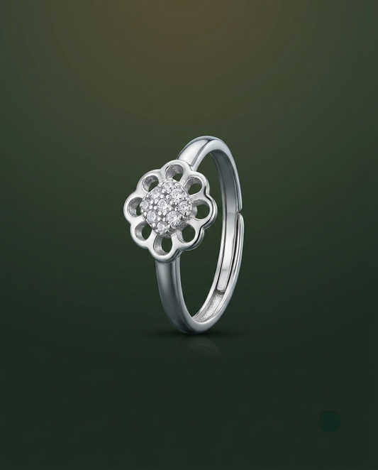 A silver flower-shaped ring with a small cluster of clear stones in the center, shown on a dark green gradient background.