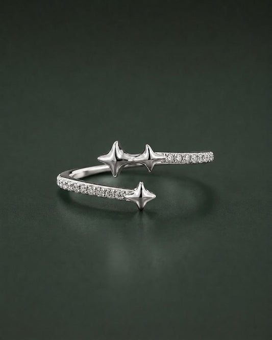 A silver open cuff ring featuring three star-shaped charms and pavé-set clear stones, displayed on a dark green reflective surface.