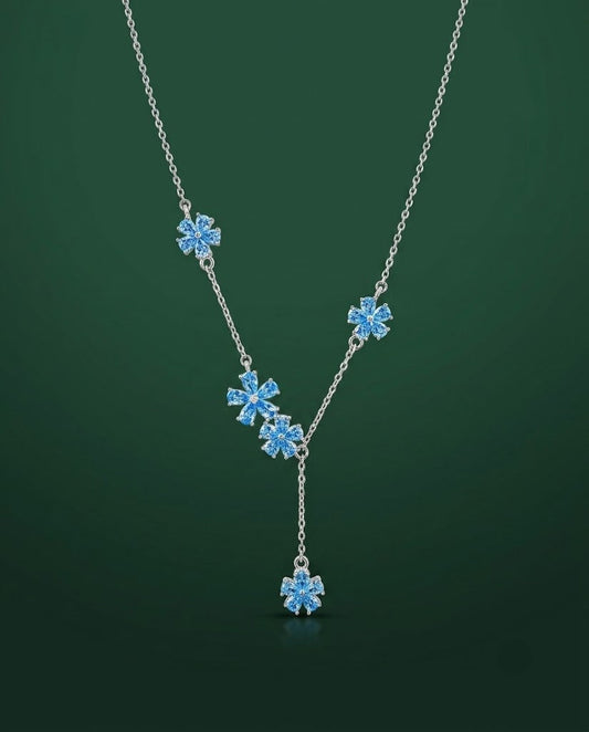 A silver Y-necklace featuring four light blue snowflake-shaped crystal charms and a matching dangling snowflake pendant, set against a dark green gradient background.