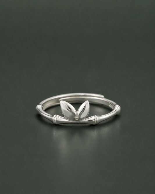 A silver ring featuring a stylized bamboo stalk design with two small leaf-like elements at the center, shown on a dark gray background.