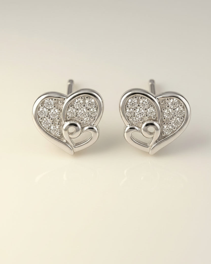 Heart-shaped silver earrings with embedded stones on a light beige background