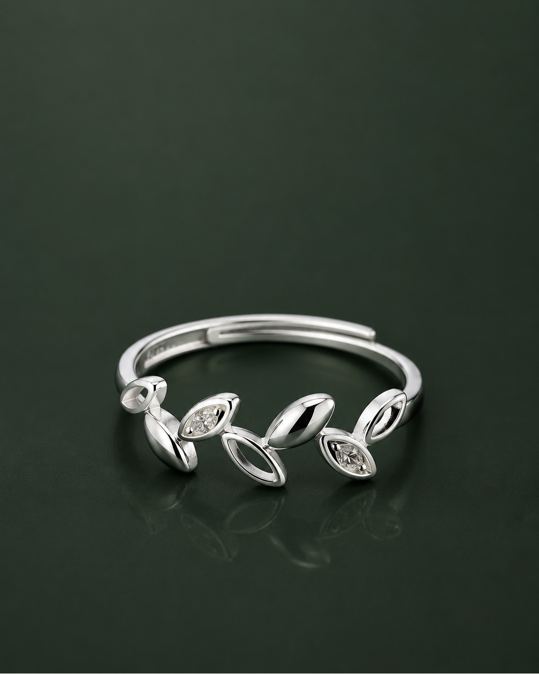 A silver adjustable ring featuring a series of stylized leaf and oval motifs, some of which are set with small clear marquise-cut stones, displayed on a dark reflective surface.