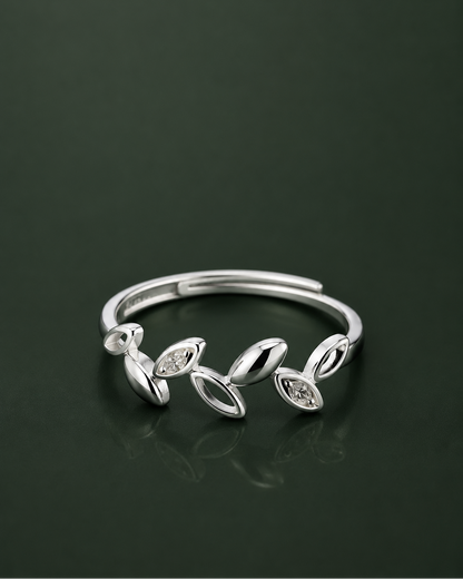 A silver adjustable ring featuring a series of stylized leaf and oval motifs, some of which are set with small clear marquise-cut stones, displayed on a dark reflective surface.