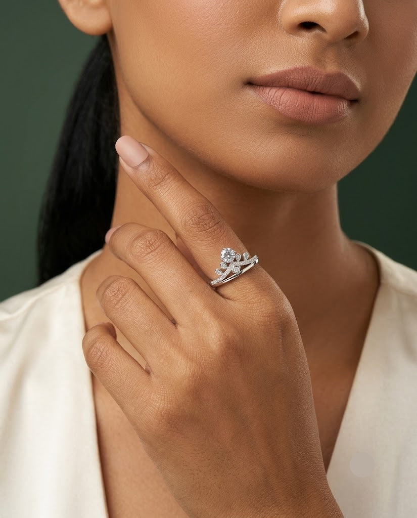 A close-up lifestyle shot of a model wearing a silver tiara-shaped ring with clear gemstones on her finger, set against a dark green background and white satin clothing.