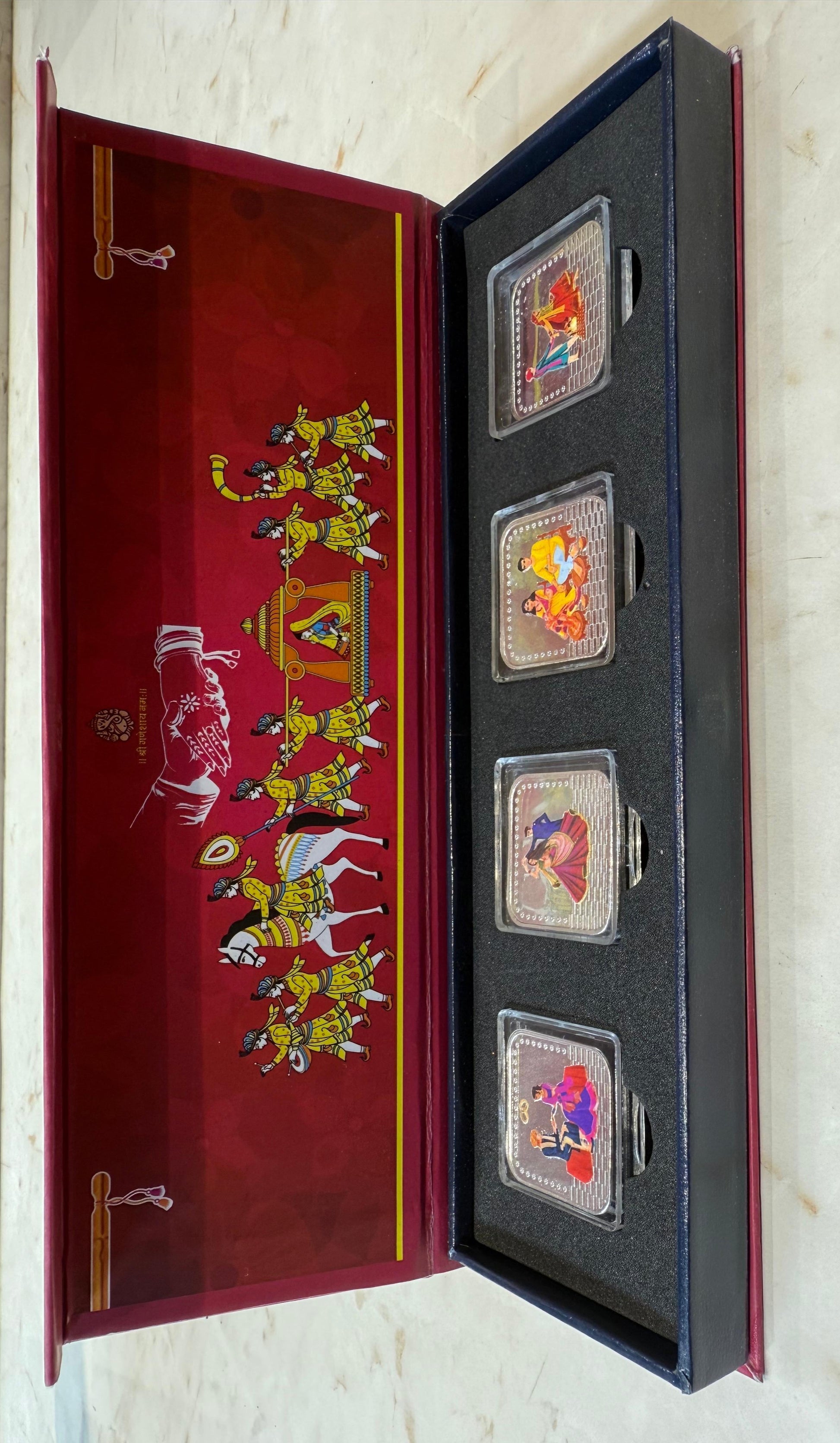 Set of four silver coins in a decorative box with illustrations on a white background