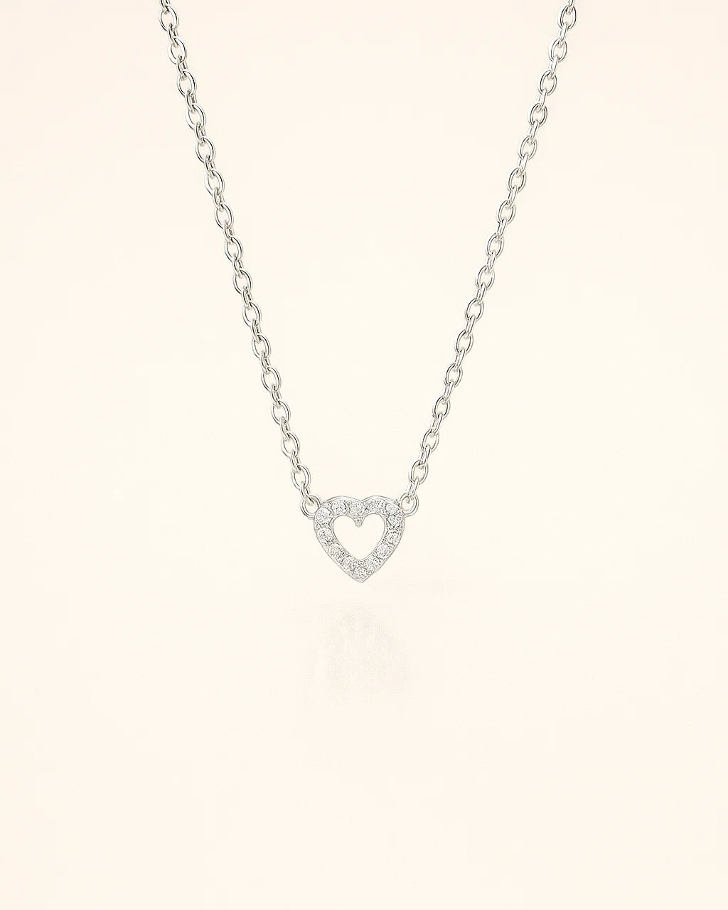 Silver necklace with a heart-shaped pendant on a light pink background
