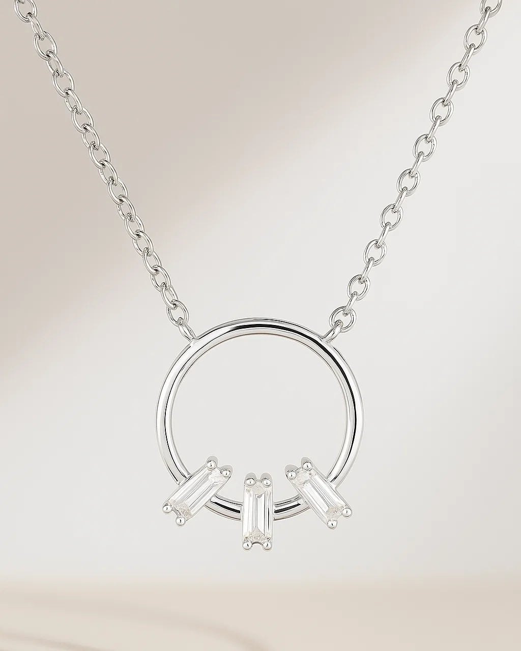 Silver necklace with circular pendant and three baguette-shaped diamonds on a beige background