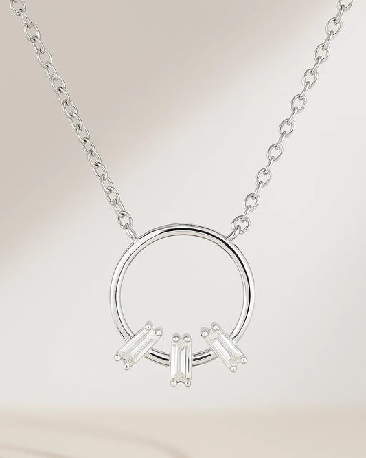 Silver necklace with circular pendant and three baguette-shaped diamonds on a beige background