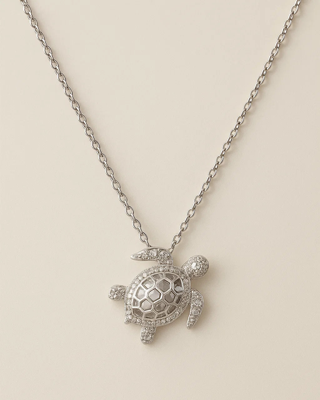 Silver turtle pendant necklace on a beige background