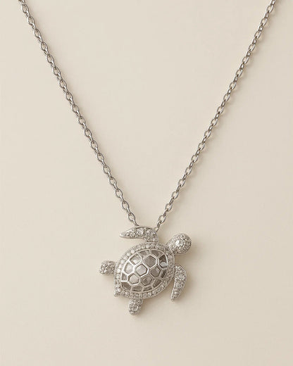 Silver turtle pendant necklace on a beige background