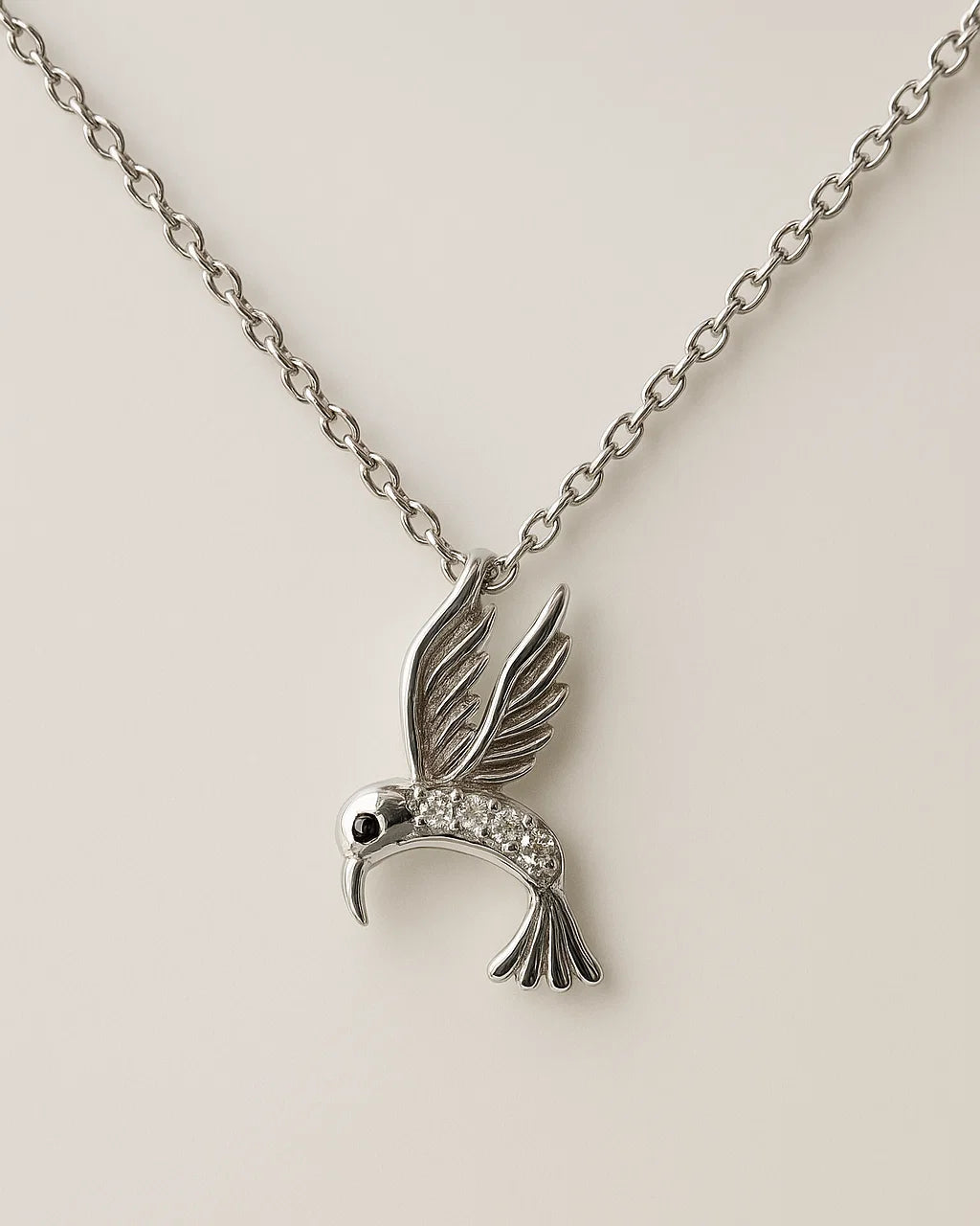 Silver hummingbird pendant necklace on a beige background