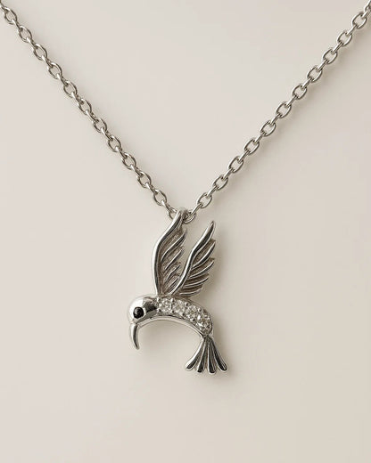 Silver hummingbird pendant necklace on a beige background