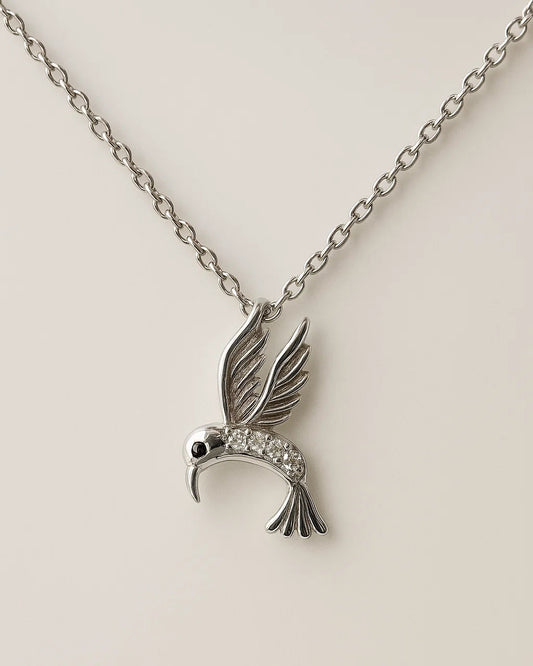 Silver hummingbird pendant necklace on a beige background
