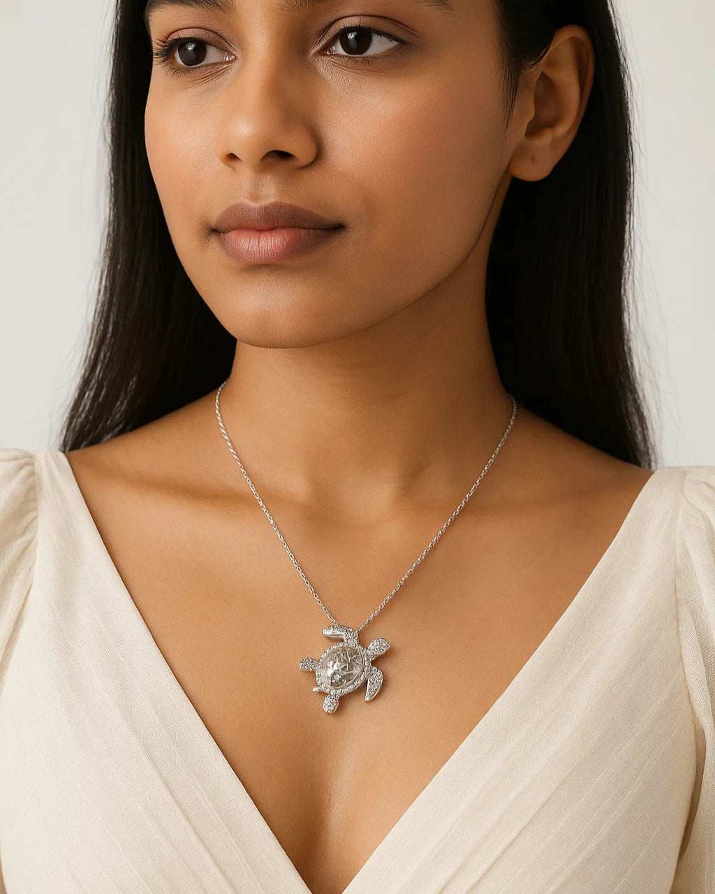 Woman wearing a necklace with a turtle pendant against a plain background
