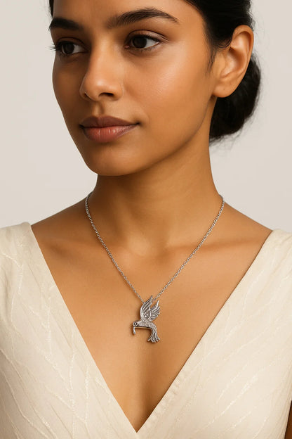 Woman wearing a silver necklace with a bird pendant on a plain background