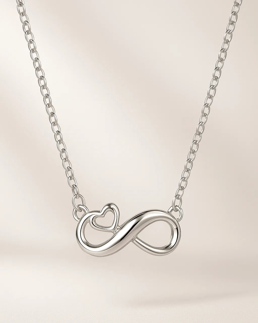 Silver infinity necklace with heart detail on a light beige background