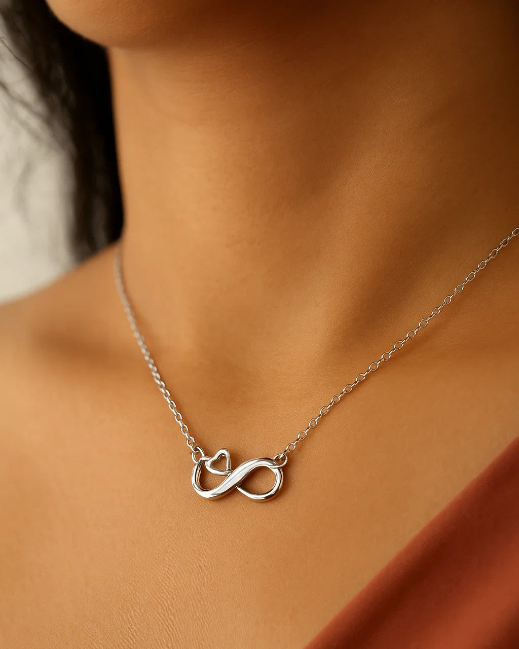 Silver infinity necklace on a person wearing a rust-colored top.