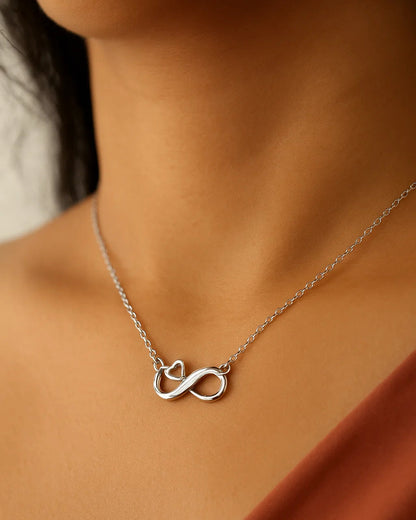 Silver infinity necklace on a person wearing a rust-colored top.