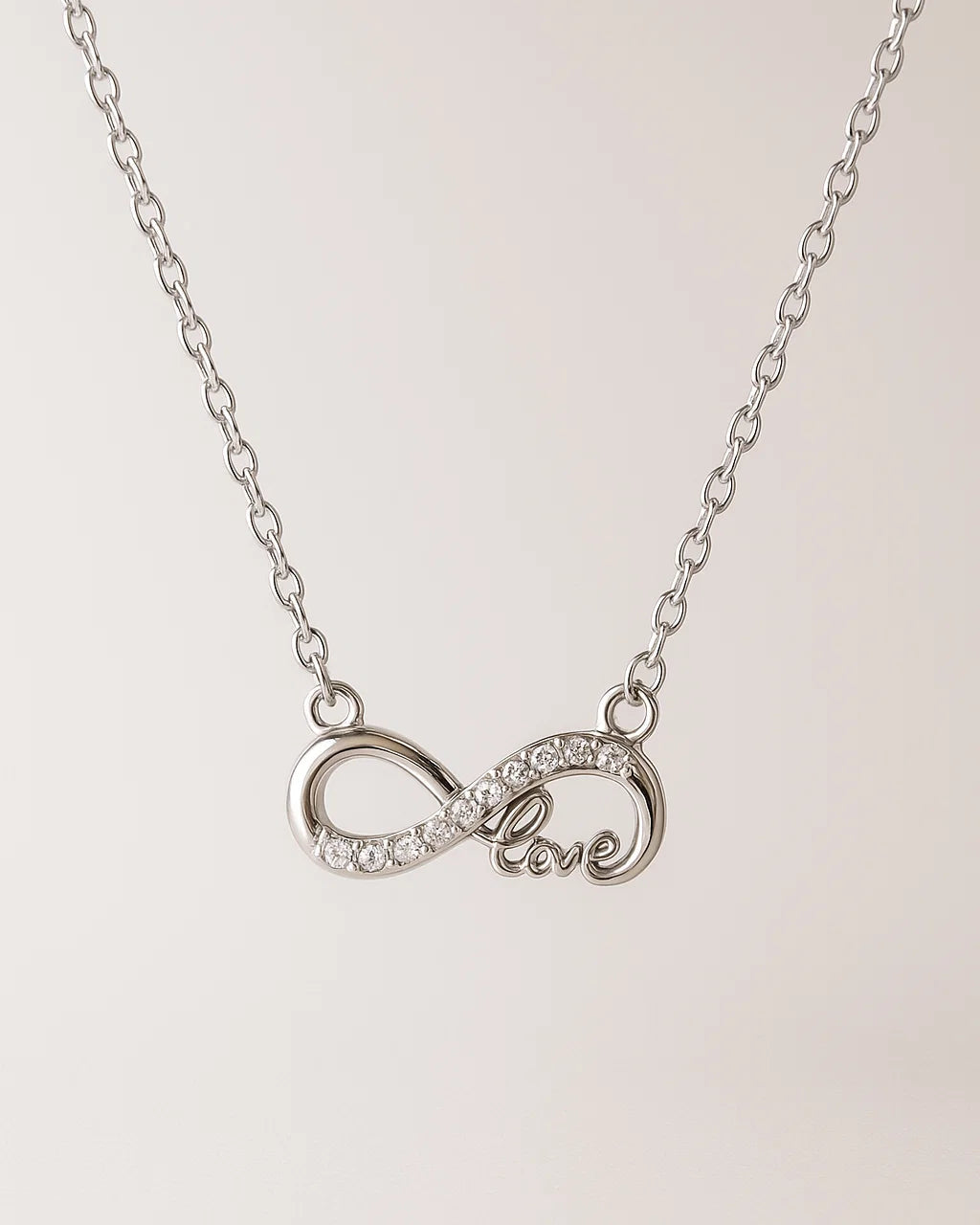 Silver necklace with an infinity symbol and 'love' engraving on a light pink background