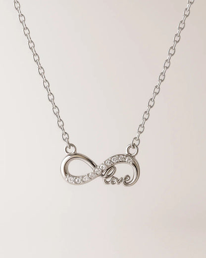 Silver necklace with an infinity symbol and 'love' engraving on a light pink background