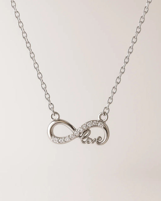 Silver necklace with an infinity symbol and 'love' engraving on a light pink background