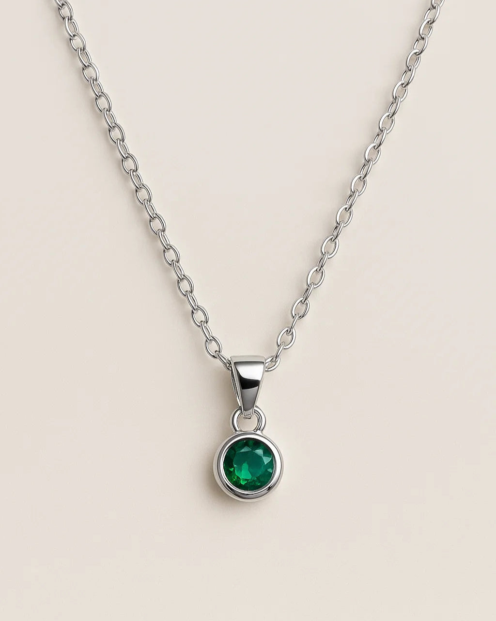 Silver necklace with a green gemstone pendant on a beige background