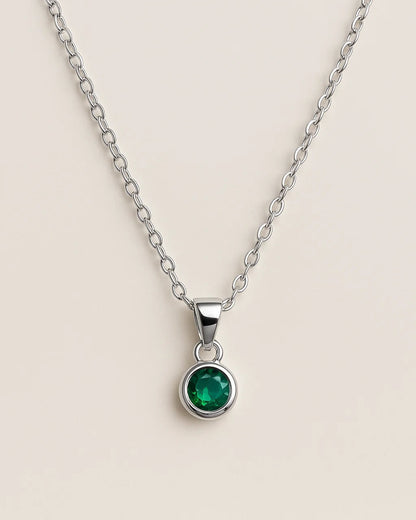 Silver necklace with a green gemstone pendant on a beige background