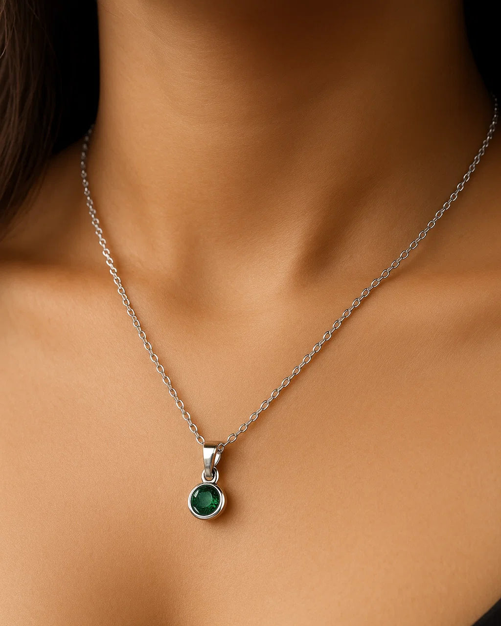 Silver necklace with a green pendant on a person wearing a black top.