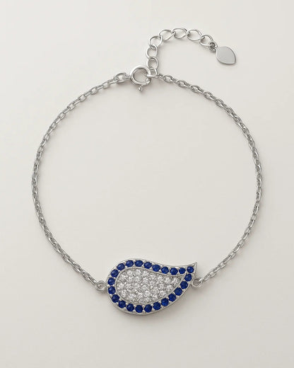 Silver bracelet with a teardrop-shaped charm featuring blue and clear stones on a light gray background.