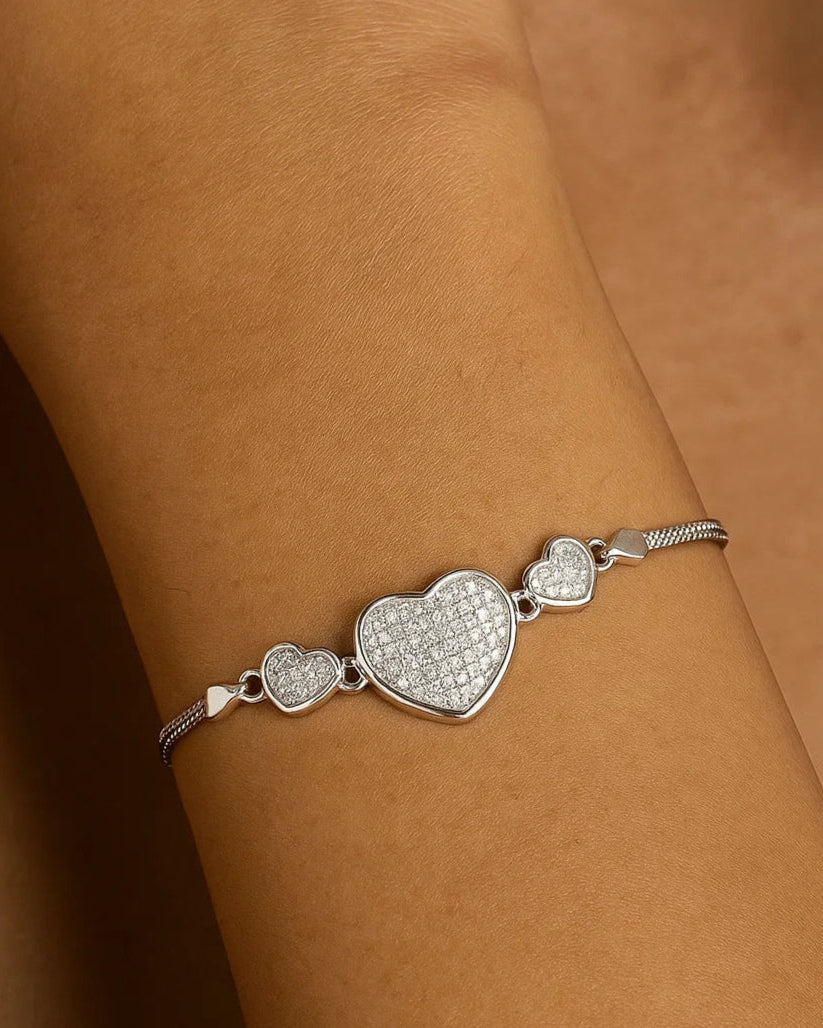 Silver bracelet with heart-shaped design on a wrist against a neutral background